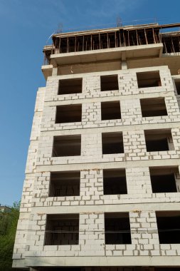 Mavi gökyüzünün arka planında yapım aşamasındaki çok katlı bir bina ve vinç.