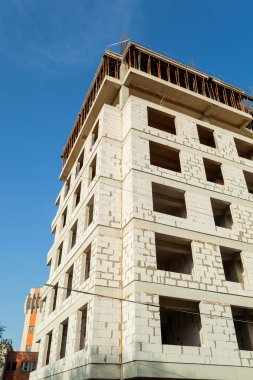 Mavi gökyüzünün arka planında yapım aşamasındaki çok katlı bir bina ve vinç.