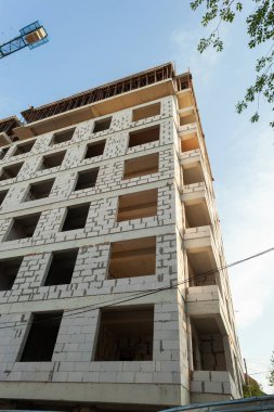 Mavi gökyüzünün arka planında yapım aşamasındaki çok katlı bir bina ve vinç.