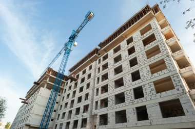 Mavi gökyüzünün arka planında yapım aşamasındaki çok katlı bir bina ve vinç.