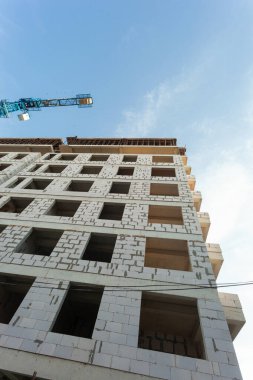 Mavi gökyüzünün arka planında yapım aşamasındaki çok katlı bir bina ve vinç.