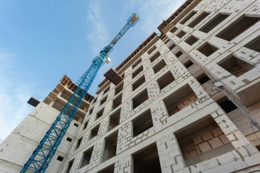 Mavi gökyüzünün arka planında yapım aşamasındaki çok katlı bir bina ve vinç.