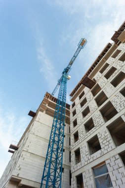 Mavi gökyüzünün arka planında yapım aşamasındaki çok katlı bir bina ve vinç.