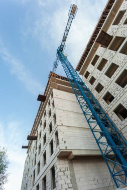 Mavi gökyüzünün arka planında yapım aşamasındaki çok katlı bir bina ve vinç.
