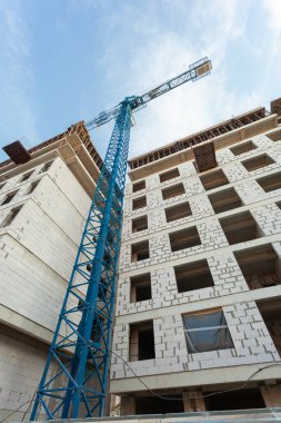 Mavi gökyüzünün arka planında yapım aşamasındaki çok katlı bir bina ve vinç.