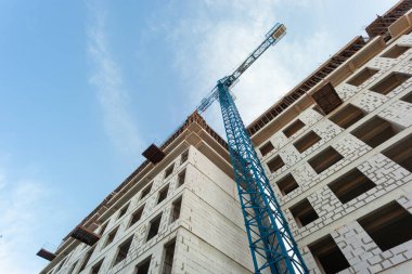 Mavi gökyüzünün arka planında yapım aşamasındaki çok katlı bir bina ve vinç.