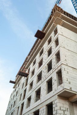 Mavi gökyüzünün arka planında yapım aşamasındaki çok katlı bir bina ve vinç.