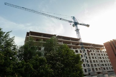 Mavi gökyüzünün arka planında yapım aşamasındaki çok katlı bir bina ve vinç.