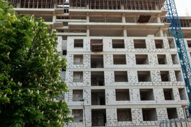 Mavi gökyüzünün arka planında yapım aşamasındaki çok katlı bir bina ve vinç.