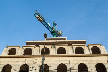 Mavi gökyüzünün arka planında yapım aşamasındaki çok katlı bir bina ve vinç.