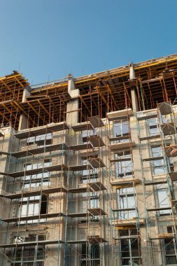 Mavi gökyüzünün arka planında yapım aşamasındaki çok katlı bir bina ve vinç.