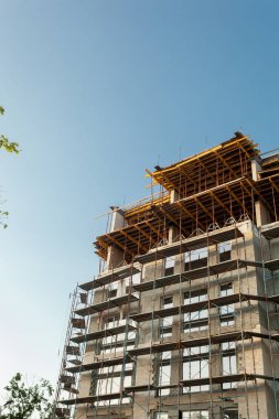 Mavi gökyüzünün arka planında yapım aşamasındaki çok katlı bir bina ve vinç.