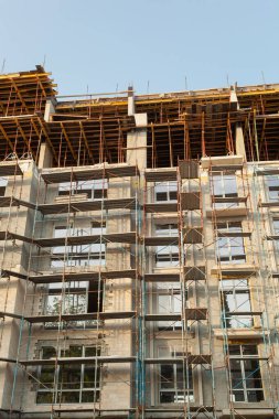 Mavi gökyüzünün arka planında yapım aşamasındaki çok katlı bir bina ve vinç.