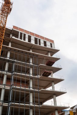 Mavi gökyüzünün arka planında yapım aşamasındaki çok katlı bir bina ve vinç.