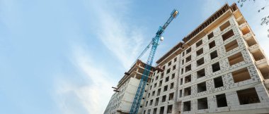 Mavi gökyüzünün arka planında inşaat halindeki çok katlı bir bina ve vinç manzarası