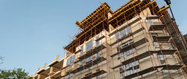 Mavi gökyüzünün arka planında inşaat halindeki çok katlı bir bina ve vinç manzarası