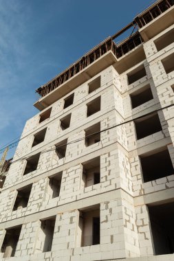 Mavi gökyüzünün arka planında yapım aşamasındaki çok katlı bir bina ve vinç.