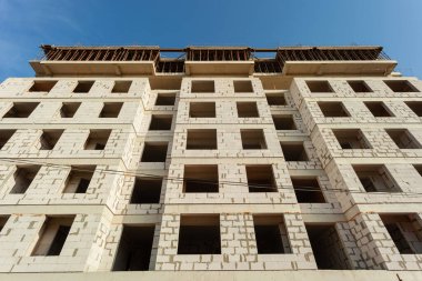 Mavi gökyüzünün arka planında yapım aşamasındaki çok katlı bir bina ve vinç.