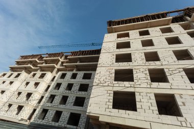 Mavi gökyüzünün arka planında yapım aşamasındaki çok katlı bir bina ve vinç.