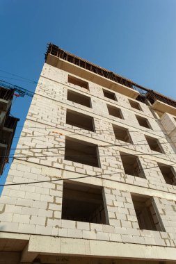 Mavi gökyüzünün arka planında yapım aşamasındaki çok katlı bir bina ve vinç.