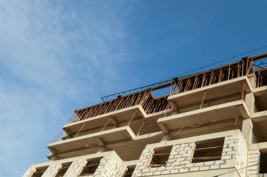 Mavi gökyüzünün arka planında yapım aşamasındaki çok katlı bir bina ve vinç.