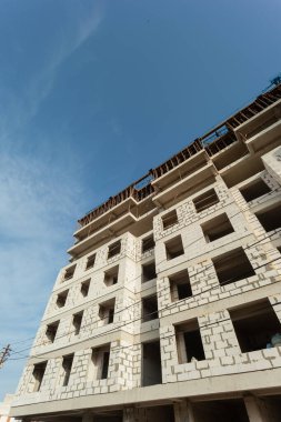 Mavi gökyüzünün arka planında yapım aşamasındaki çok katlı bir bina ve vinç.