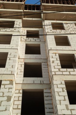 Mavi gökyüzünün arka planında yapım aşamasındaki çok katlı bir bina ve vinç.