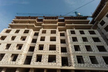 Mavi gökyüzünün arka planında yapım aşamasındaki çok katlı bir bina ve vinç.