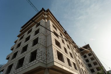 Mavi gökyüzünün arka planında yapım aşamasındaki çok katlı bir bina ve vinç.