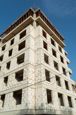 Mavi gökyüzünün arka planında yapım aşamasındaki çok katlı bir bina ve vinç.