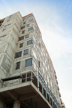 Mavi gökyüzünün arka planında yapım aşamasındaki çok katlı bir bina ve vinç.