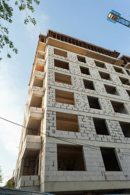 Mavi gökyüzünün arka planında yapım aşamasındaki çok katlı bir bina ve vinç.