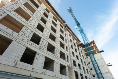 Mavi gökyüzünün arka planında yapım aşamasındaki çok katlı bir bina ve vinç.