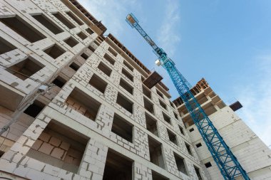 Mavi gökyüzünün arka planında yapım aşamasındaki çok katlı bir bina ve vinç.