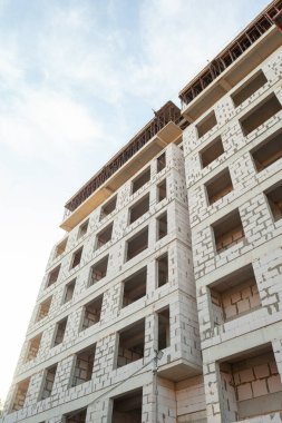 Mavi gökyüzünün arka planında yapım aşamasındaki çok katlı bir bina ve vinç.