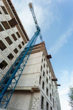 Mavi gökyüzünün arka planında yapım aşamasındaki çok katlı bir bina ve vinç.