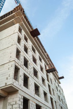 Mavi gökyüzünün arka planında yapım aşamasındaki çok katlı bir bina ve vinç.