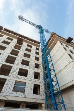 Mavi gökyüzünün arka planında yapım aşamasındaki çok katlı bir bina ve vinç.