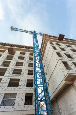 Mavi gökyüzünün arka planında yapım aşamasındaki çok katlı bir bina ve vinç.