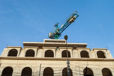 Mavi gökyüzünün arka planında yapım aşamasındaki çok katlı bir bina ve vinç.