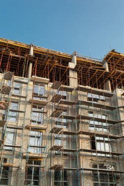 Mavi gökyüzünün arka planında yapım aşamasındaki çok katlı bir bina ve vinç.