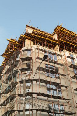 Mavi gökyüzünün arka planında yapım aşamasındaki çok katlı bir bina ve vinç.