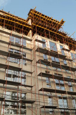 Mavi gökyüzünün arka planında yapım aşamasındaki çok katlı bir bina ve vinç.