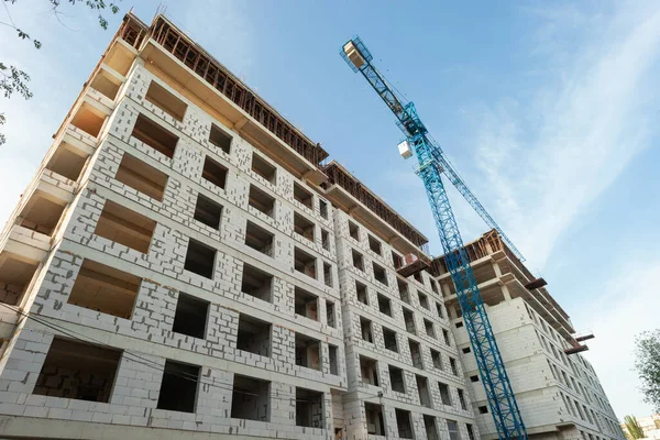 Mavi gökyüzünün arka planında yapım aşamasındaki çok katlı bir bina ve vinç.