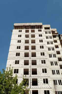 Mavi gökyüzünün arka planında yapım aşamasındaki çok katlı bir bina ve vinç.