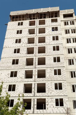 Mavi gökyüzünün arka planında yapım aşamasındaki çok katlı bir bina ve vinç.