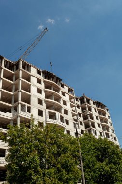 Mavi gökyüzünün arka planında yapım aşamasındaki çok katlı bir bina ve vinç.