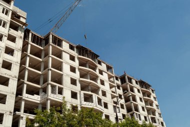 Mavi gökyüzünün arka planında yapım aşamasındaki çok katlı bir bina ve vinç.