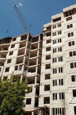 Mavi gökyüzünün arka planında yapım aşamasındaki çok katlı bir bina ve vinç.