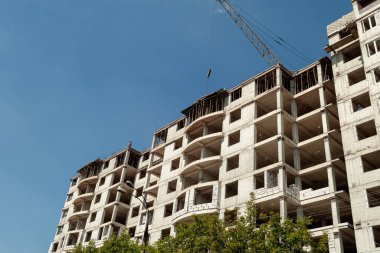 Mavi gökyüzünün arka planında yapım aşamasındaki çok katlı bir bina ve vinç.